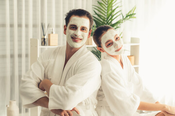Blissful couple in bathrobe with facial cream mask enjoying serene ambiance of spa salon resort or...