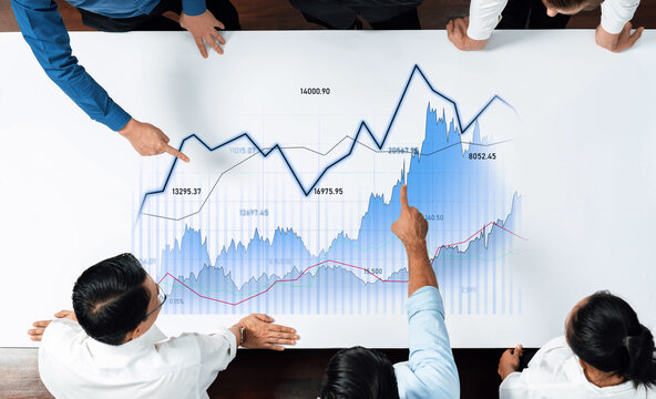 A diverse group of business professionals examines financial charts and graphs on a table, showcasing teamwork and analysis of stock market trends in a modern office setting. Scalp