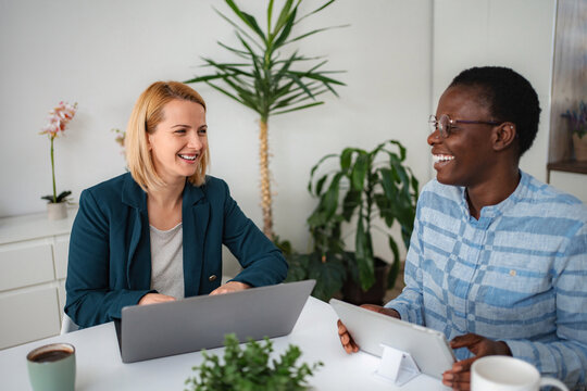 Diverse businesswomen collaborating smiling using laptop and tablet in office