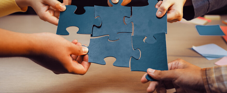 Diverse hands join together to connect blue puzzle pieces on a wooden surface, representing the spirit of teamwork, collaboration, and joint problem-solving efforts. SACTR