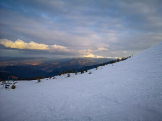 Scenic winter mountain landscape with snowy slope panoramic view soft sunset clouds and distant peaks in calm natural atmosphere.