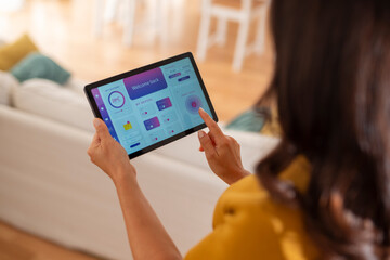 Woman using a smart home control app on a digital tablet at home.  

