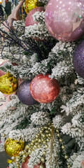 Festive Christmas tree decorated with pink, gold, and purple baubles on snowy pine branches creating a cozy holiday mood. Selective focus