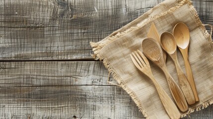 Wooden kitchen utensils including a fork and three spoons arranged on a rustic cloth on a wooden table.