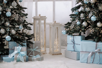 Decorated Christmas trees with blue and silver baubles and wrapped gifts on white wooden floor. Concept of winter holidays, celebration, cozy home interior.