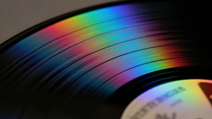 closeup of black vinyl record with iridescent rainbow spectrum reflecting on its surface. detailed concentric grooves create abstract texture. retro music and analog audio concept.
