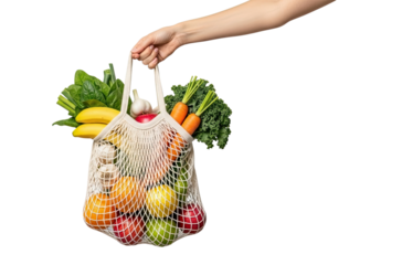 A female hand holds a reusable mesh shopping bag full of fresh organic fruits and vegetables like carrots, kale, and apples, isolated on a solid black background