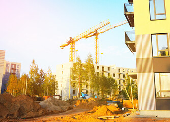 New apartment complex under construction on bright sky background. Construction workers build condo apartment. Tower cranes on buildings construction. Construction site with tower cranes in build.