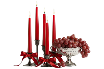 A romantic and festive arrangement of five burning red taper candles in silver candlesticks and an ornate bowl of ripe grapes isolated on a solid black background
