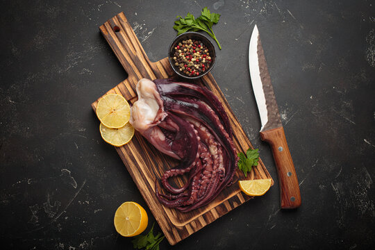 Fresh raw octopus or squid preparing for a seafood meal, placed on a wooden cutting board with lemon and a knife