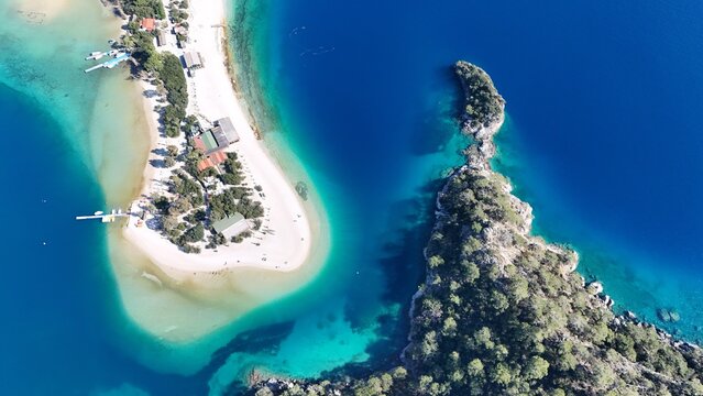 A drone view of the Ölüdeniz peninsula and its turquoise lagoon on the Mediterranean coast of Turkey, surrounded by forested mountains and clear blue water. - Powered by Adobe