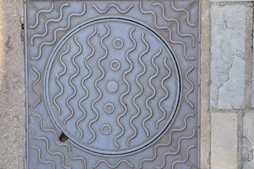 Decorative metal manhole cover with circular waves and geometric pattern.