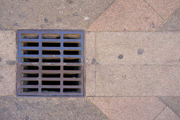 Metal street drain grate embedded in a stone pavement.