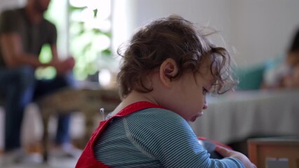Toddler deeply engaged while inspecting helmet up close, carefully moving it around with intent curiosity, creating peaceful moment of early learning, gentle focus, and quiet home exploration