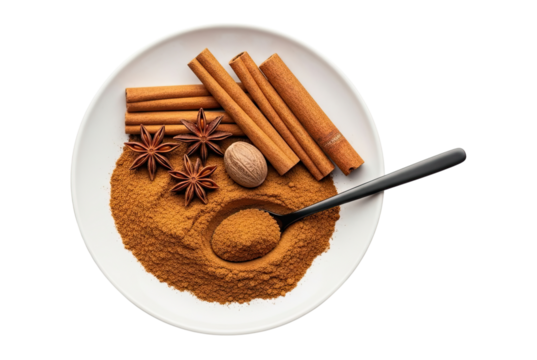 Top view flat lay of aromatic baking spices like cinnamon sticks and powder, star anise, and nutmeg on a white plate with a spoon, isolated on a clean black background