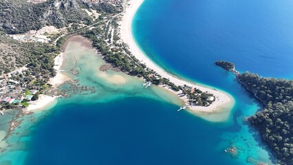 A drone view of the Ölüdeniz peninsula and its turquoise lagoon on the Mediterranean coast of Turkey, surrounded by forested mountains and clear blue water.