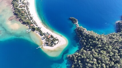 A drone view of the Ölüdeniz peninsula and its turquoise lagoon on the Mediterranean coast of Turkey, surrounded by forested mountains and clear blue water.
