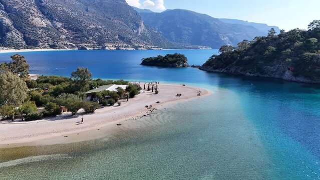 A drone view of the Ölüdeniz peninsula and its turquoise lagoon on the Mediterranean coast of Turkey, surrounded by forested mountains and clear blue water. - Powered by Adobe