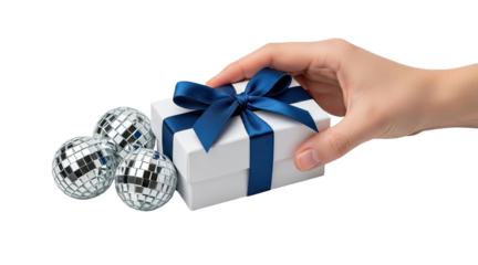 A person's hand holds a white gift box with a blue satin ribbon next to shiny disco balls, creating a festive and celebratory concept isolated on a black background