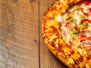 A cooked pizza with a lot of toppings including chicken, peppers, and onions. The pizza is sitting on a wooden table. Fine Italian style meal popular world wide. Rich dough base.