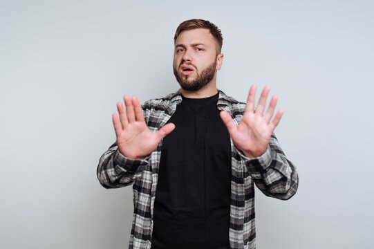 portrait of young man adopts a defensive posture by raising his hands on white background
