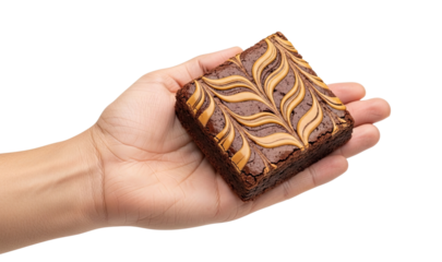 A person's hand holds a delicious homemade chocolate brownie with a beautiful peanut butter swirl pattern on top, isolated on a clean black background in a studio setting