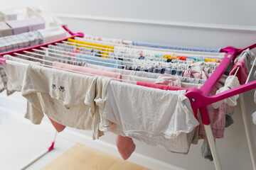 Fresh laundry hangs from a drying rack indoors, captured from below to emphasize dangling fabrics, colorful pins, and the organized structure of the household air-drying setup