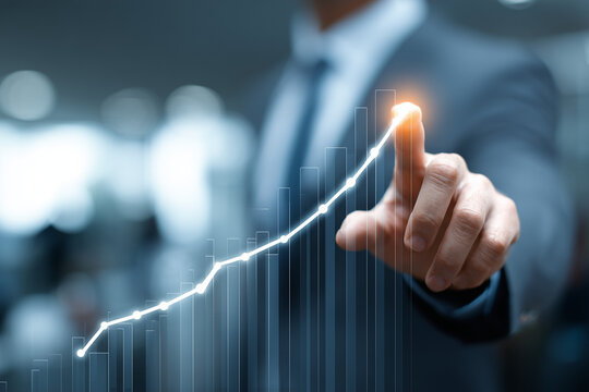 A business professional is pointing at a digital growth chart that shows an upward trend. This activity is taking place in a modern office setting, emphasizing progress and success