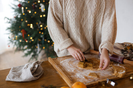 Making holiday cookies. Woman making christmas gingerbread cookies close up on rustic table with rolling pin, fir branches, candle and metal cutters against christmas tree in evening - Powered by Adobe