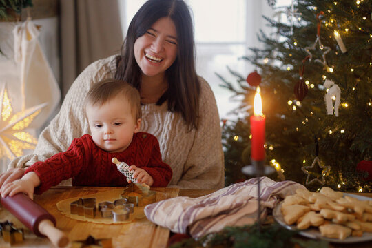 Joyful family making gingerbread christmas cookies on table with dough and metal cutters against christmas tree lights. Mom and son together. Merry Christmas and happy holidays
