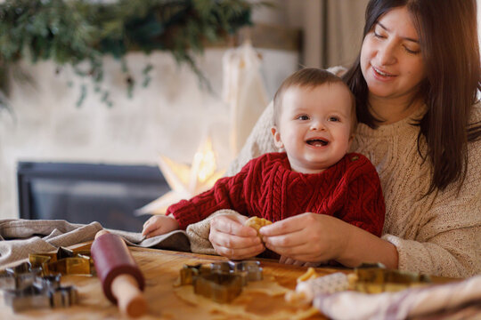 Joyful family making gingerbread christmas cookies on table with dough and metal cutters against fireplace. Mom and son together. Merry Christmas and happy holidays