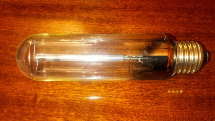 A clear, cylindrical high-pressure sodium lamp bulb resting horizontally on a dark wooden surface