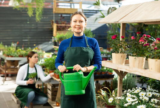 Woman florist seller holding green watering can in flower shop..