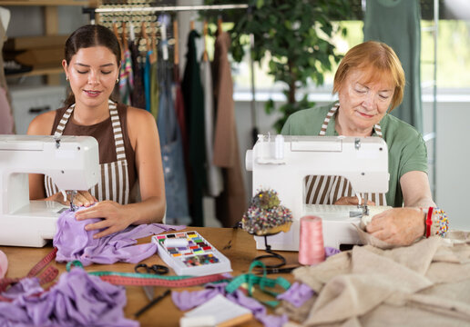 Experienced seamstress works in a team with an assistant, they sew clothes in the workshop. Dressmakers sew fabric on sewing machines