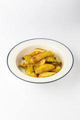 Golden roasted potato wedges with fresh herbs in a bowl on white background