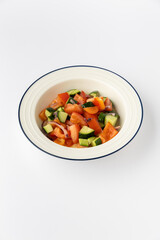 Fresh chopped tomato cucumber salad with red onion and pepper in white bowl, studio isolated