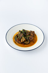 Beef stew with eggplant in tomato sauce, garnished with herbs, studio plate on white