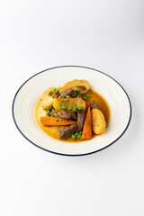Beef stew with potatoes, carrots and peas in rich gravy on a white plate