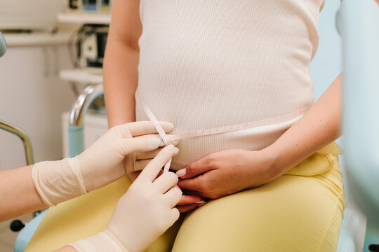 Gynecologist checks size of the woman belly in the clinic. Gynecologist measures pregnant belly with measuring tape to follow the growth of the baby on the appointment.