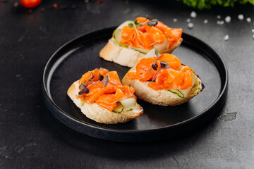 Gourmet salmon canapes on baguette with cream cheese and cucumber on black plate