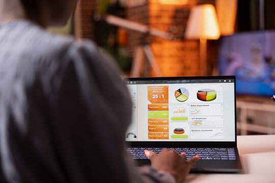 Laptop screen shows business analytics as african american woman reviews data and prepares reports at home. Focused female freelancer develops marketing strategies using digital device on desk. - Powered by Adobe