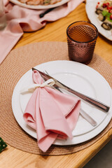 Elegant place setting with pink napkin and ribbon on woven placemat, wedding dinner decor