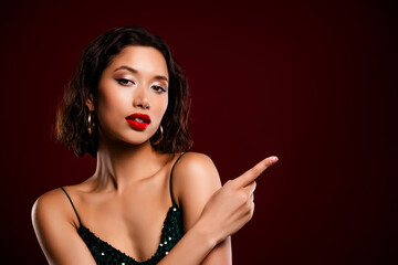 Glamorous young woman in a green sequined dress posing confidently against a red background