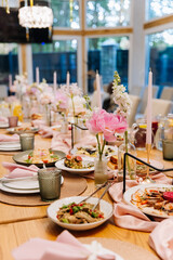 Elegant banquet table with pink peonies, taper candles and plates set for celebration