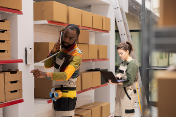 Black male staff member in coveralls manages phone calls about custom orders, ensuring dispatch...