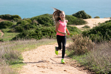 Young girl dressed in bright sport clothes are jogging on cliffs along the ocean