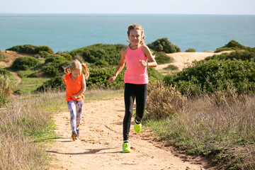 Two young ladies dressed in bright sport clothes are jogging on cliffs along the ocean 