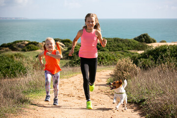 Two young ladies dressed in bright sport clothes are jogging with a dog on cliffs along the ocean 