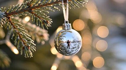 Silver bauble reflects peaceful winter scene on frosted branch, surrounded by festive lights, capturing holiday magic and cheer