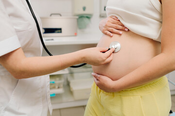 Pregnancy checkup. Gynecologist with stethoscope listening baby heartbeat in patient tummy on...